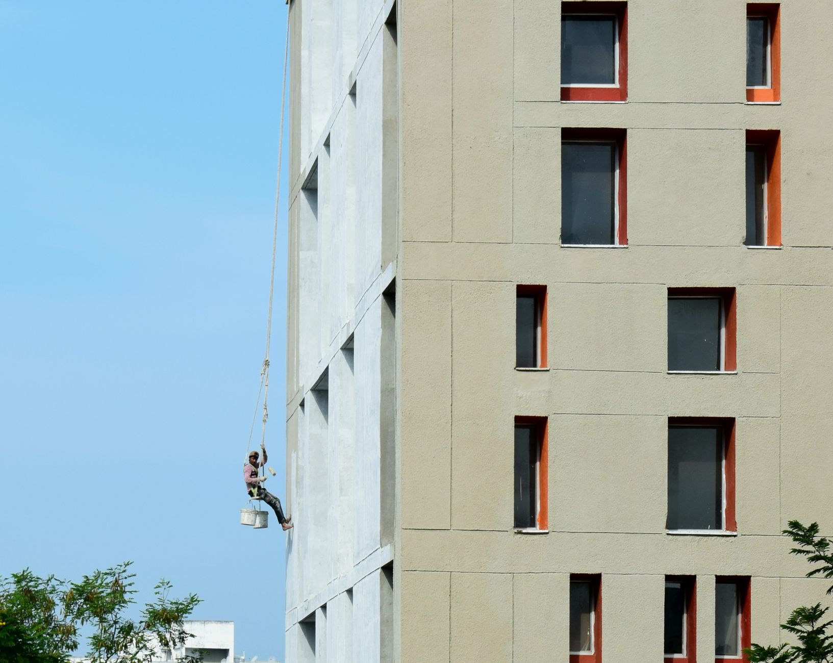 A painter suspended on a building facade, painting a high-rise structure in Carlsbad, CA